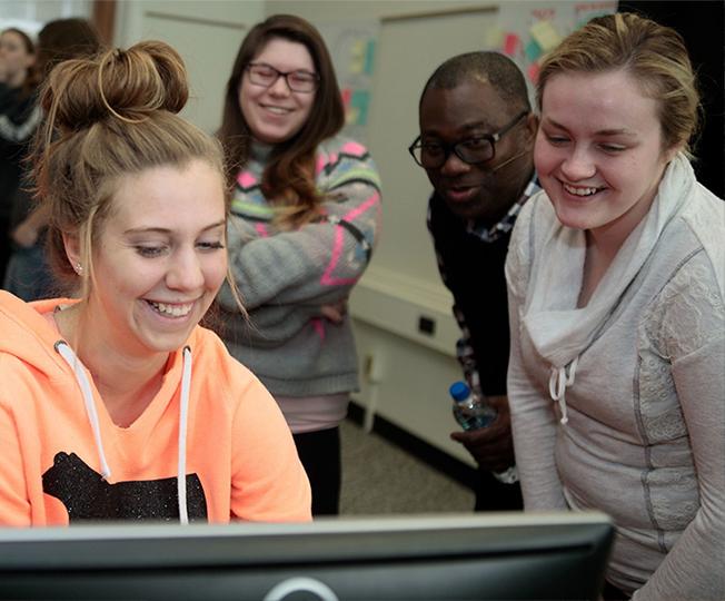 Students around a computer screen smiling